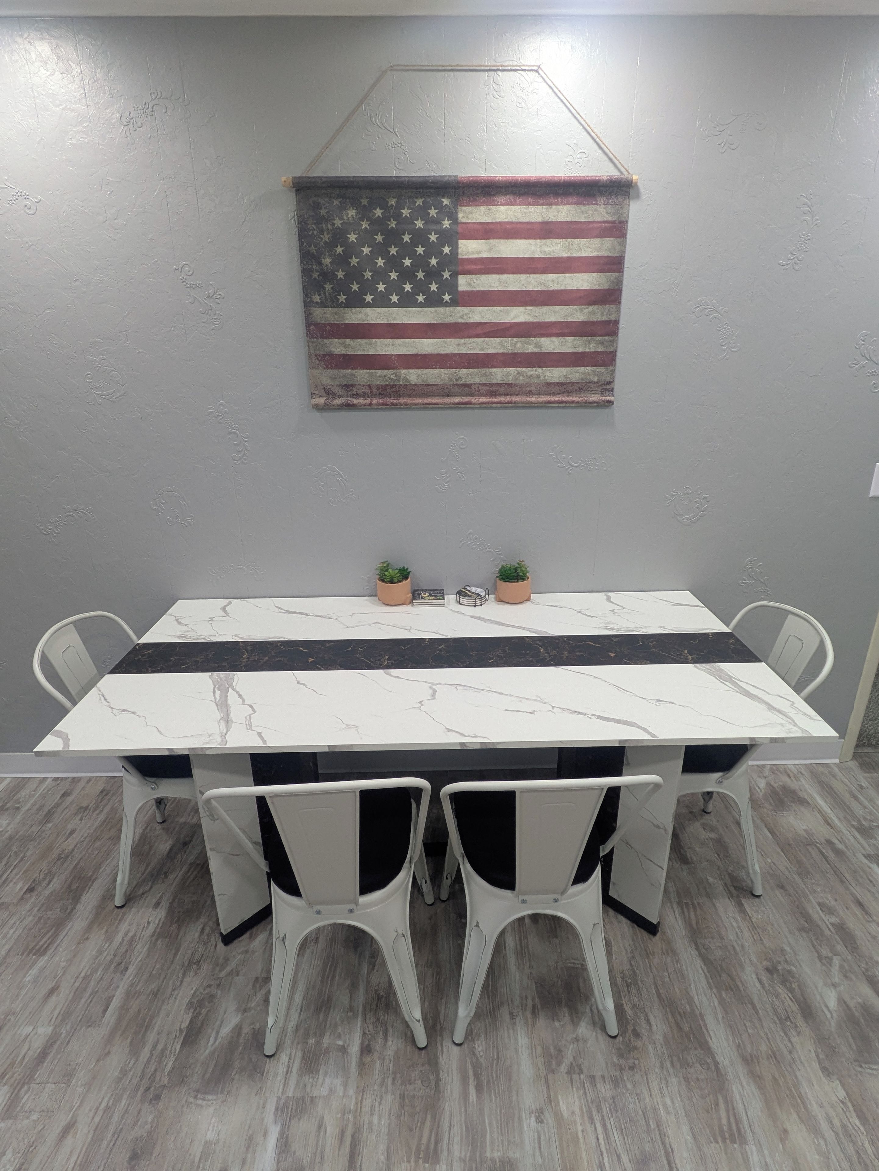 Een eethoek met een tafel en stoelen, een decoratie met de Amerikaanse vlag, en een behang met een patroon.