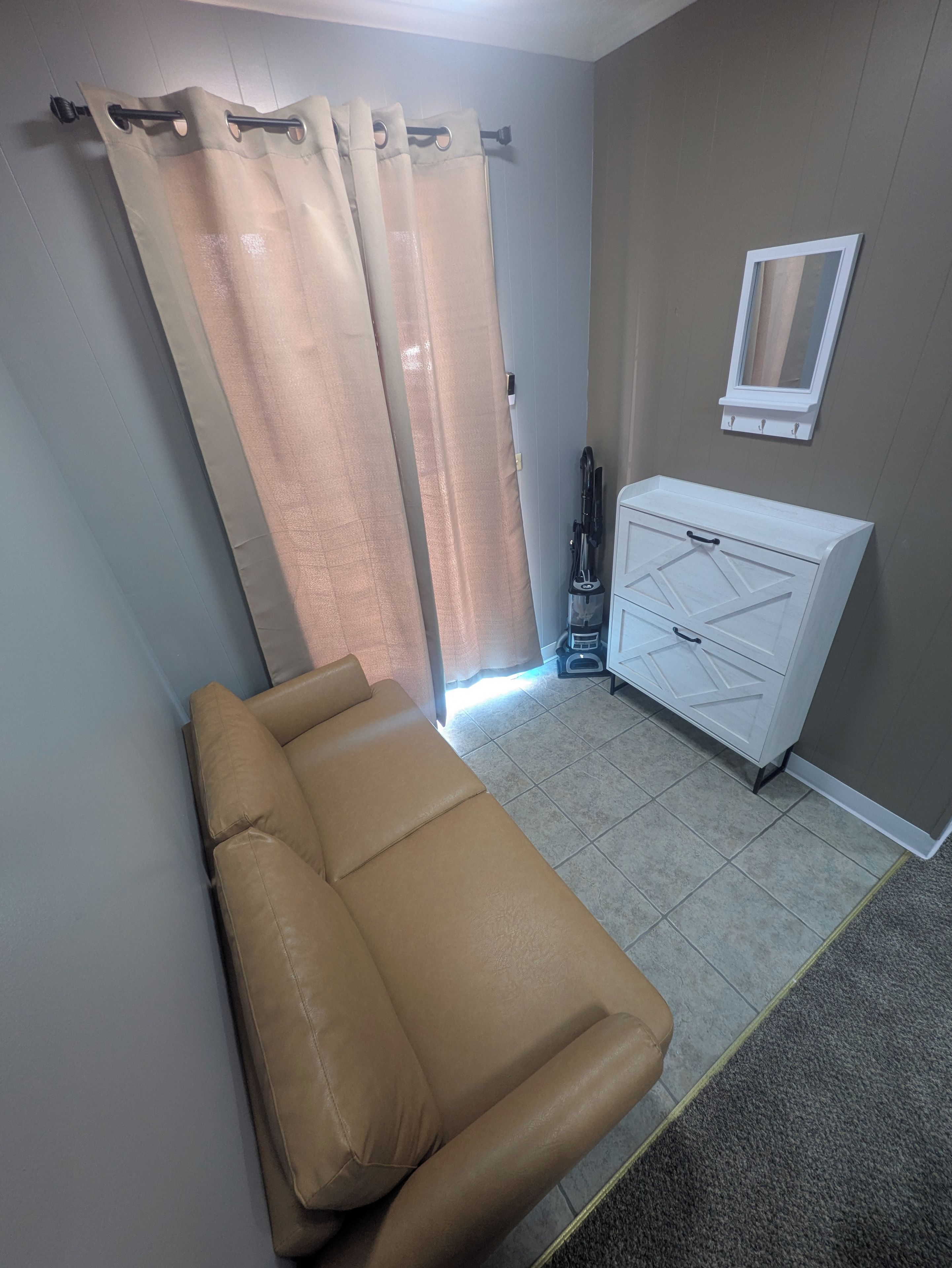 A room with a single bed, a white cabinet, a mirror, and a curtain.