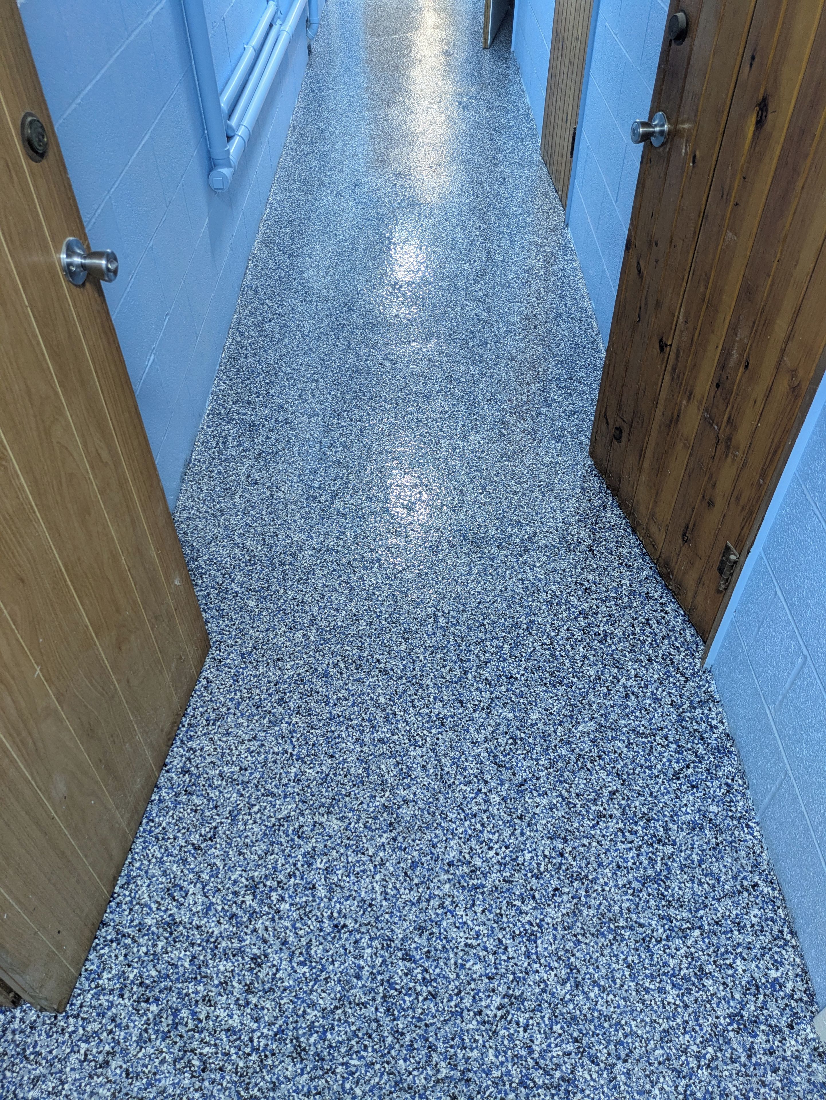 Un couloir avec un sol à motifs, des portes en bois et des murs bleus.