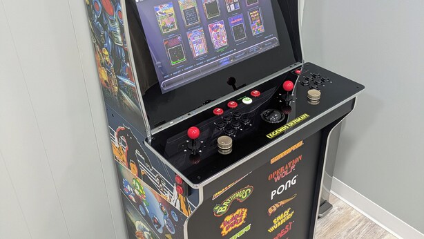Máquina de videojuegos con pantalla que muestra opciones de juego, controles de joystick y una selección de títulos a un lado.