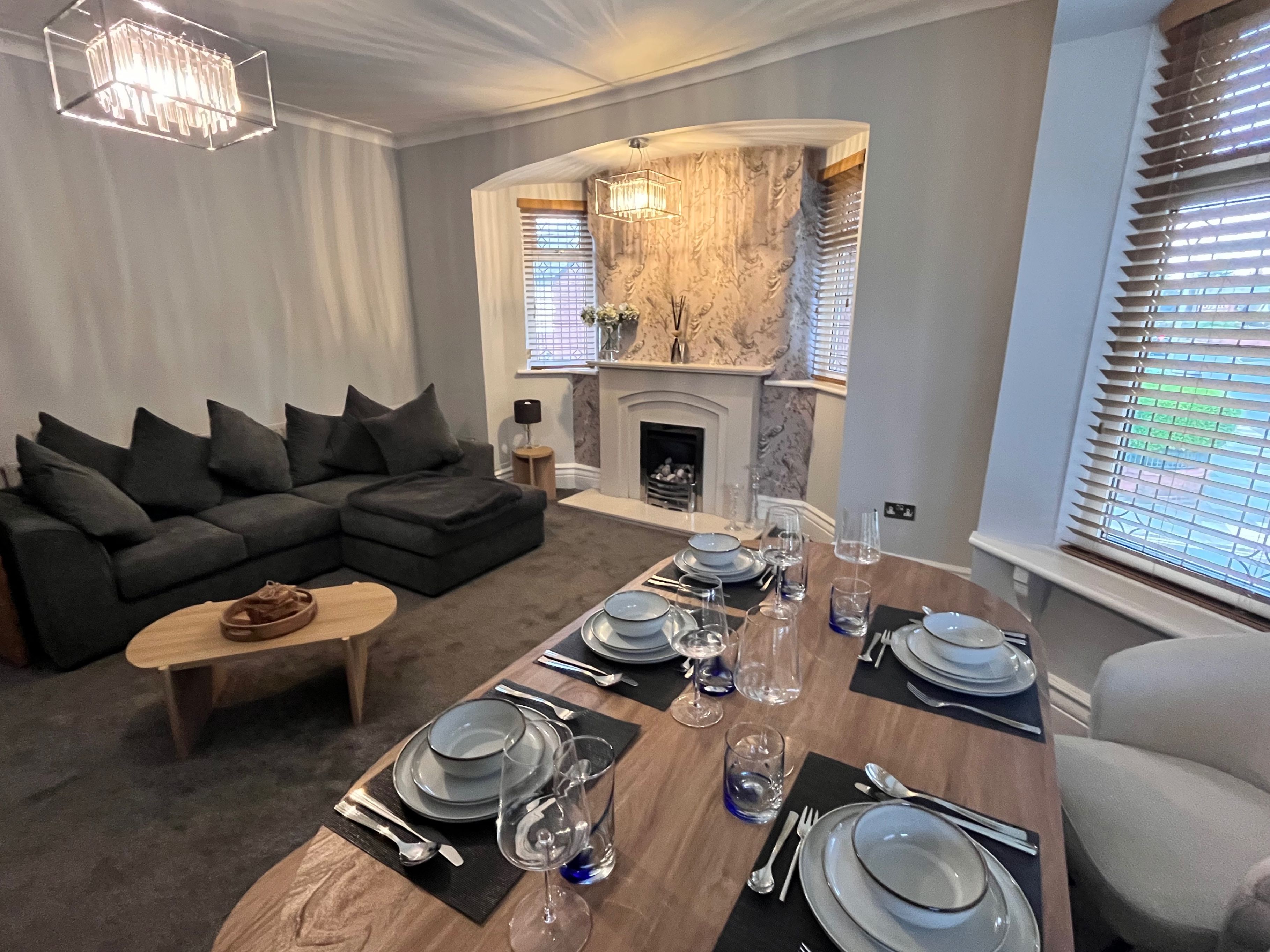 A modern living room with a sectional sofa, a dining table set for four, and a fireplace.