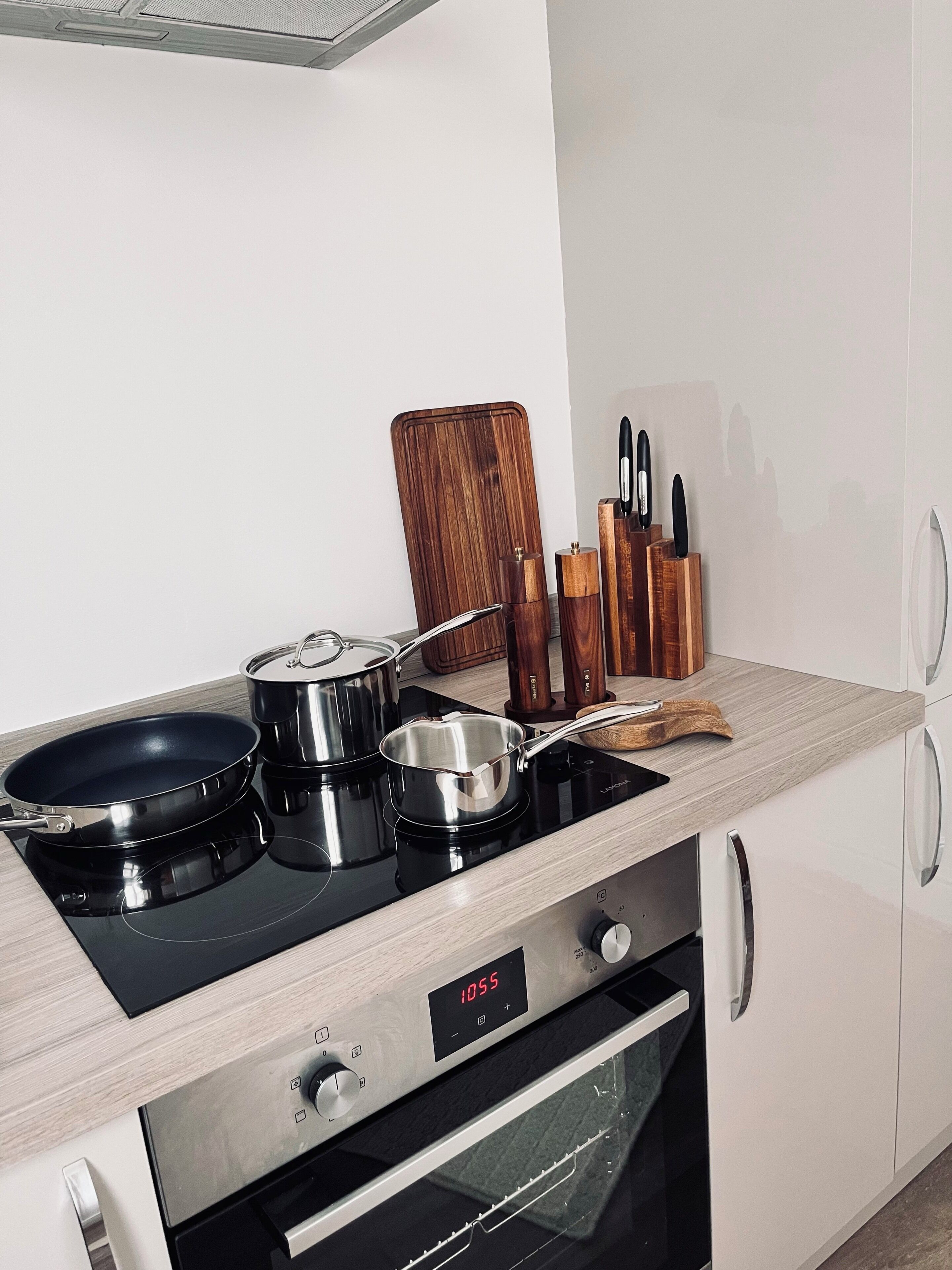 A modern kitchen with a stove, pots, a frying pan, and a digital clock.