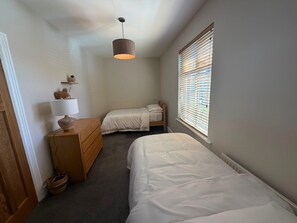 A small, well-lit bedroom with a single bed, a dresser, a lamp, and a window with blinds. - 3 Bedroom Apartment 2 up to 5 People Free Parking (Blackpool)