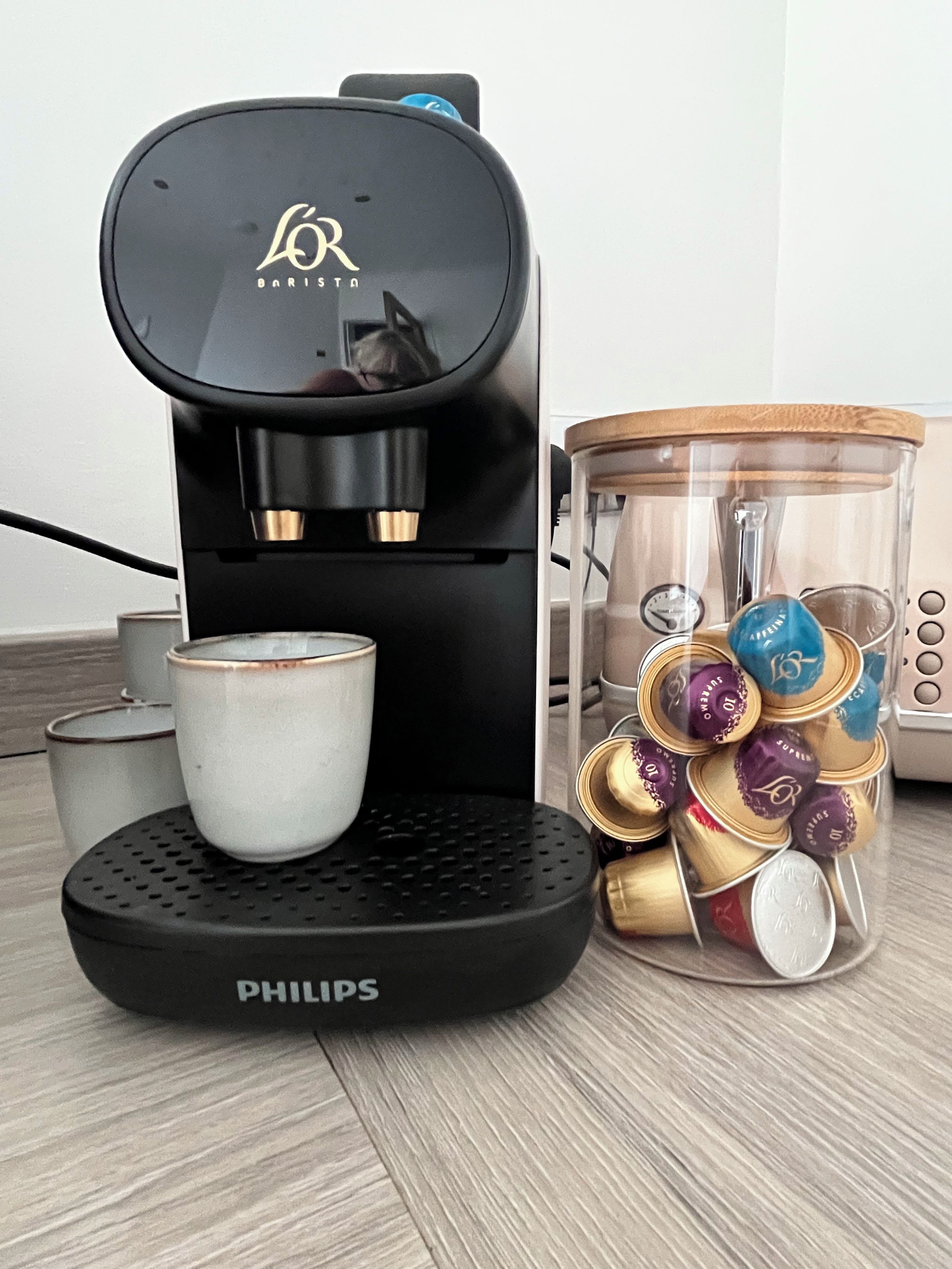 A coffee maker with a cup and a container of coffee capsules.
