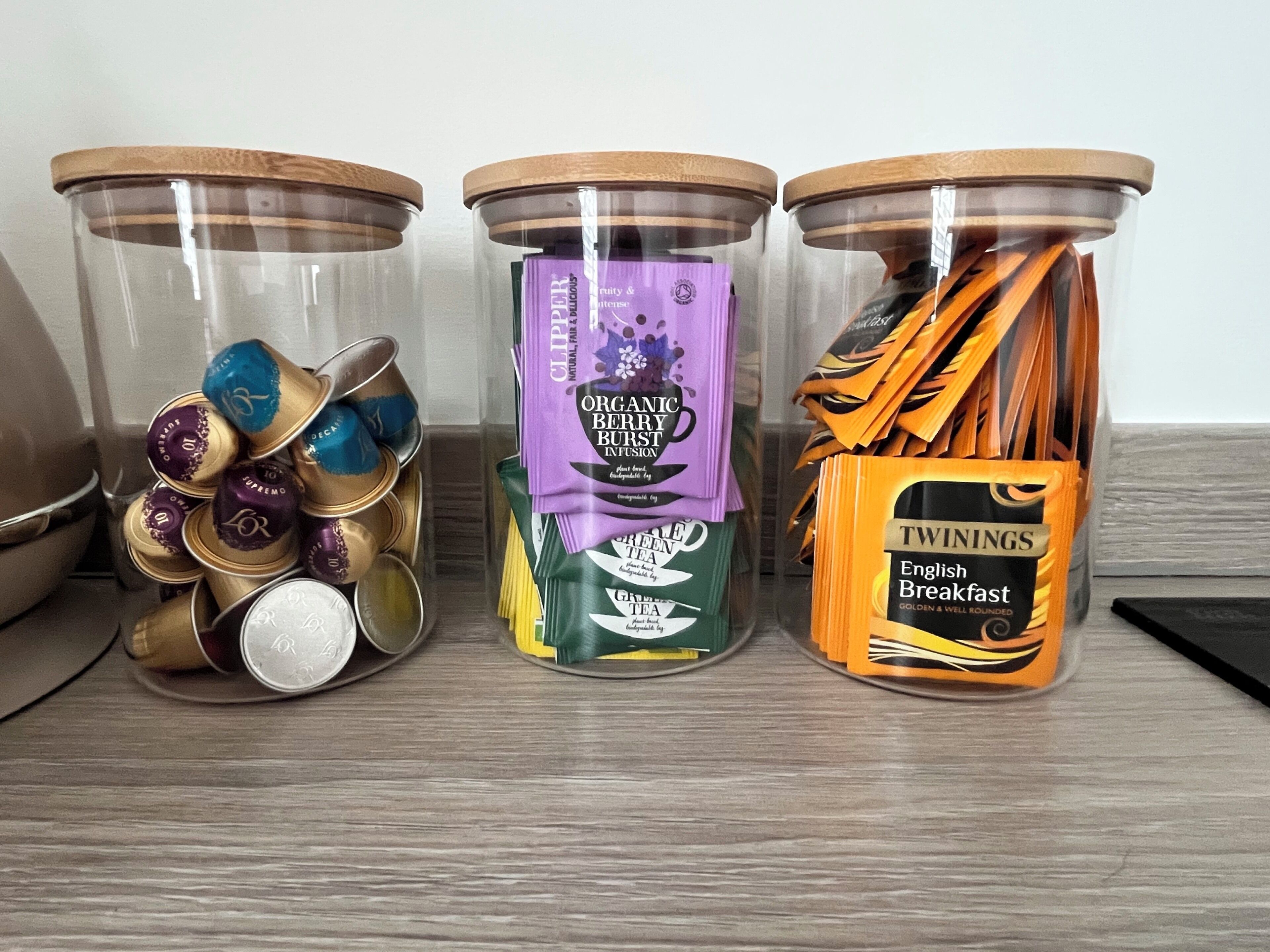 Trois bocaux en verre, dotés de couvercles en bois, contenant différents types d’aliments.