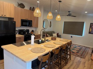 A modern kitchen with wooden cabinets, a black refrigerator, and a central island with bar stools. - New Tucson home for travel nurses, grads & professionals, near hospitals" (Tucson)
