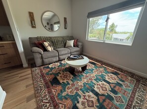 A living room with a grey sofa, a round coffee table, a patterned rug, a large window, and a mirror on the wall. - New Tucson home for travel nurses, grads & professionals, near hospitals" (Tucson)