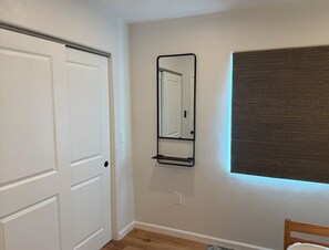 Une pièce avec une porte blanche, un miroir fixé au mur et une fenêtre avec un store marron.