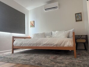 Une chambre à coucher avec un lit en bois, un tapis gris, un climatiseur et un haut-parleur fixé au mur.