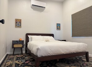 A neatly made bed with white linens, a dark wooden headboard, a small bedside table with a lamp, and a patterned rug on the floor. - New Tucson home for travel nurses, grads & professionals, near hospitals" (Tucson)