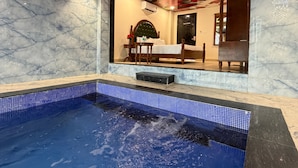 Ein Hotelzimmer mit Marmorboden, einem Pool mit blauen Fliesen und Blick auf einen Speisebereich mit Tisch und Stühlen.