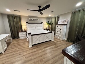 Een slaapkamer met een bed, nachtkastjes, een bureau, een plafondventilator en een muur met een motiverende quote.