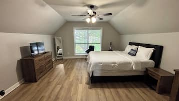 Een slaapkamer met een schuine kap, een bed met witte beddengoed, een dressoir, een spiegel en een plafondventilator.
