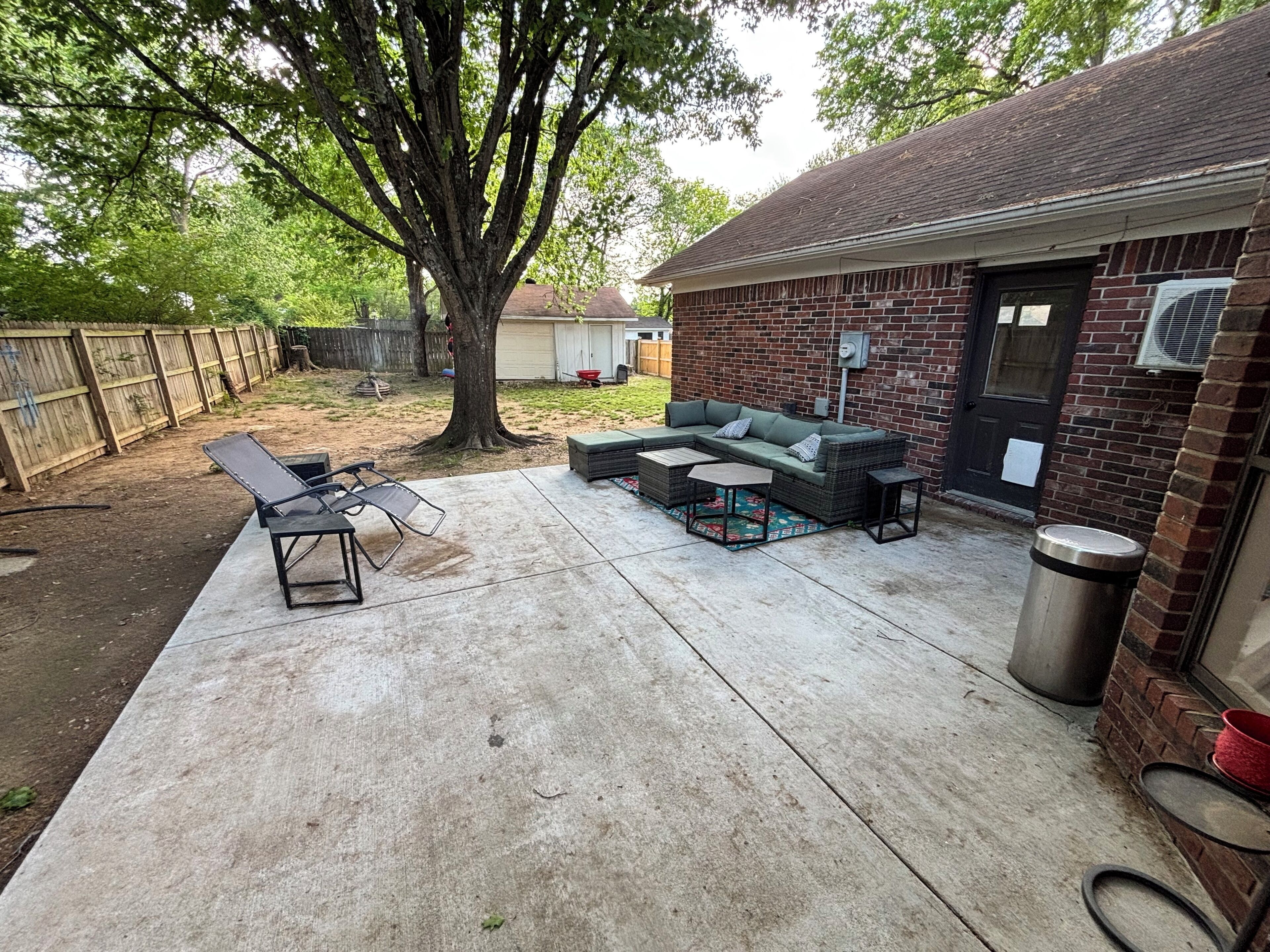 A backyard patio with a sectional sofa, a dining table, and a trash can.