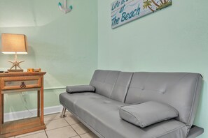 Una stanza con un divano grigio, un tavolino in legno con una lampada e un'decorazione a tema spiaggia.