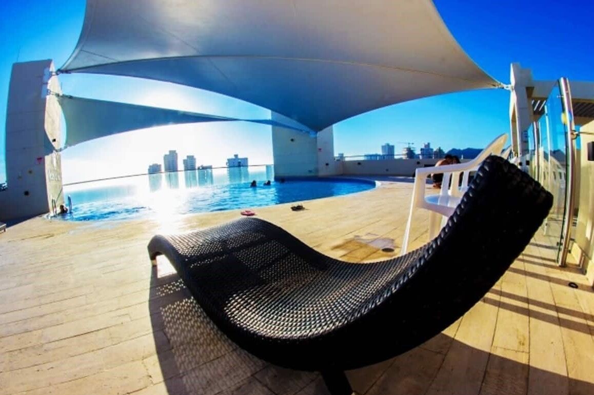 A sunlit outdoor area with a pool, lounge chairs, and a view of the city skyline.