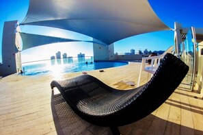 Ein sonniger Außenbereich mit Pool, Liegestühlen und Blick auf die Stadtlandschaft.