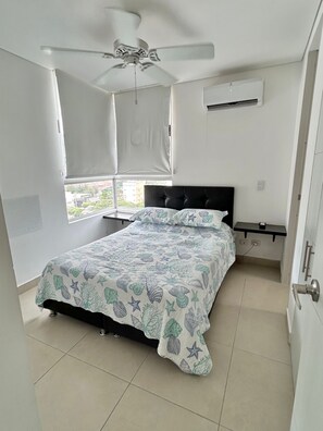Ein Schlafzimmer mit einem Bett, Deckenventilator, Fenster mit Jalousien, Klimaanlage und Nachttisch.