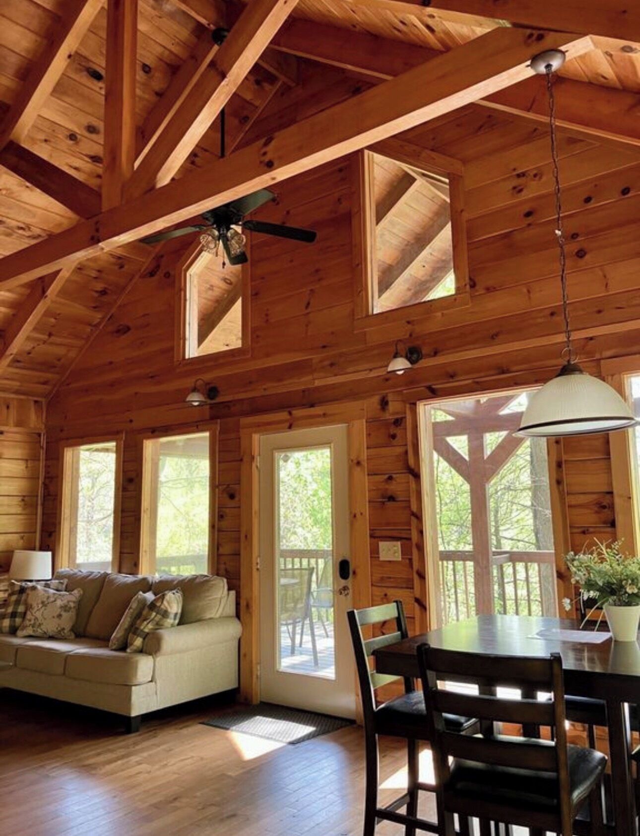 L’intérieur d’un chalet en bois, avec un canapé, une table à manger, des chaises et un ventilateur de plafond.