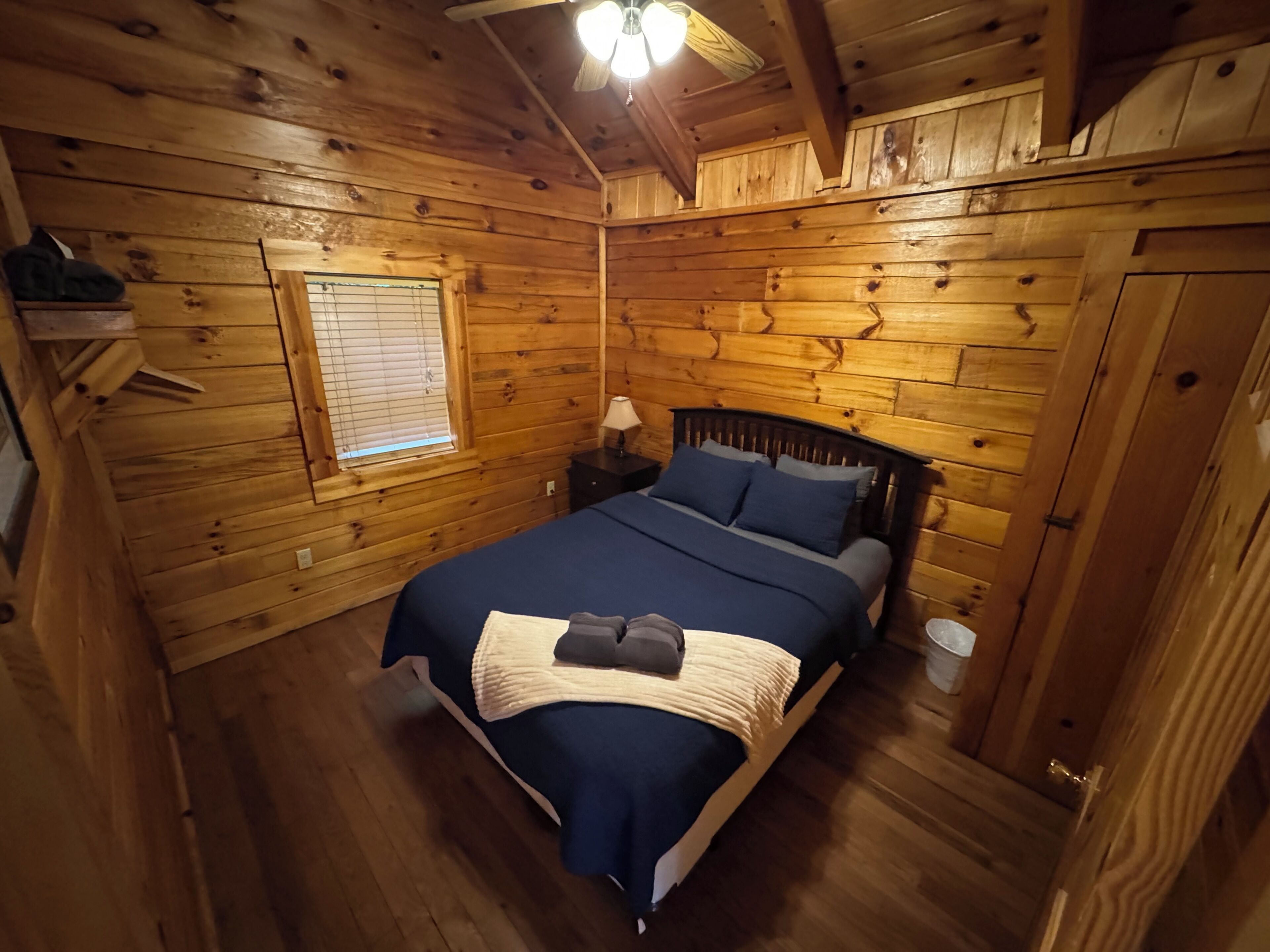 A wooden cabin bedroom with a bed, nightstands, and a window.
