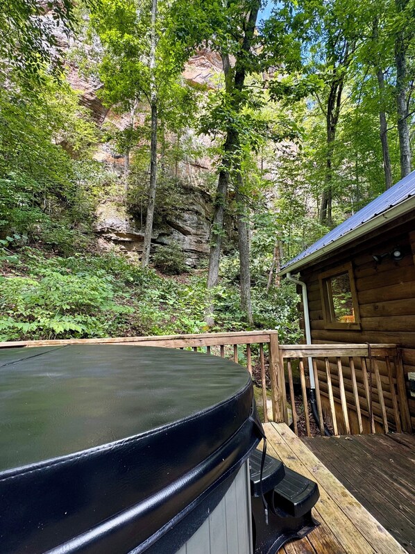 A hot tub on a wooden deck with a view of a forested cliff.