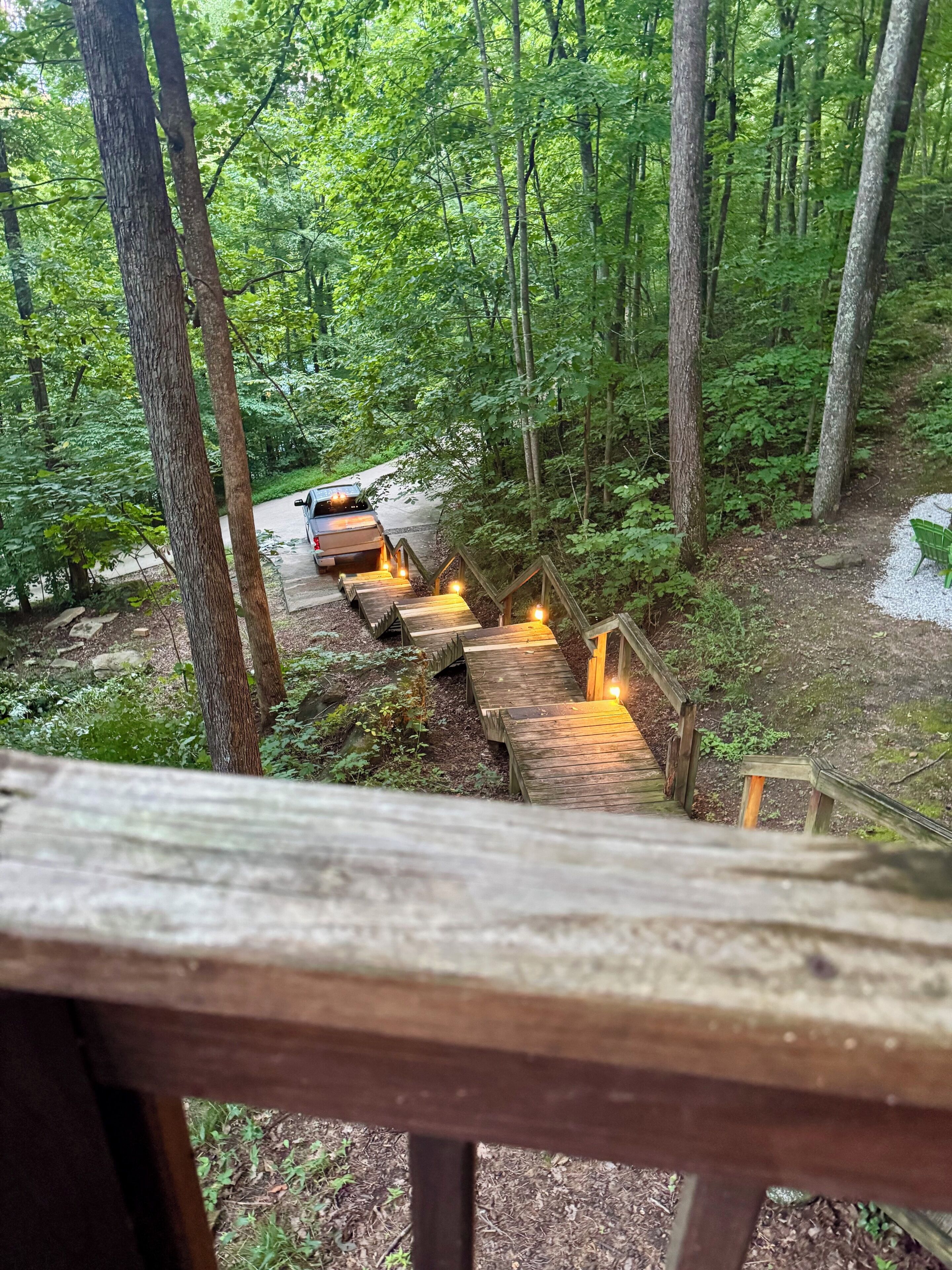 A wooden staircase leading into a forested area with a vehicle parked at the top.