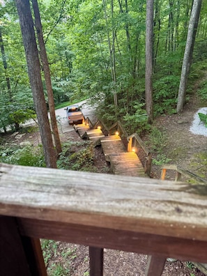 A wooden staircase leading into a forested area with a vehicle parked at the top.