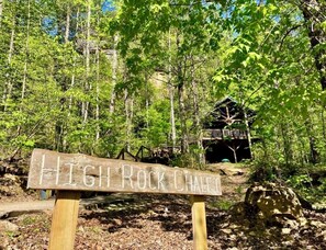 A wooden sign with 'HIGH ROCK CHALET' written on it, surrounded by a forest with a cabin in the background.