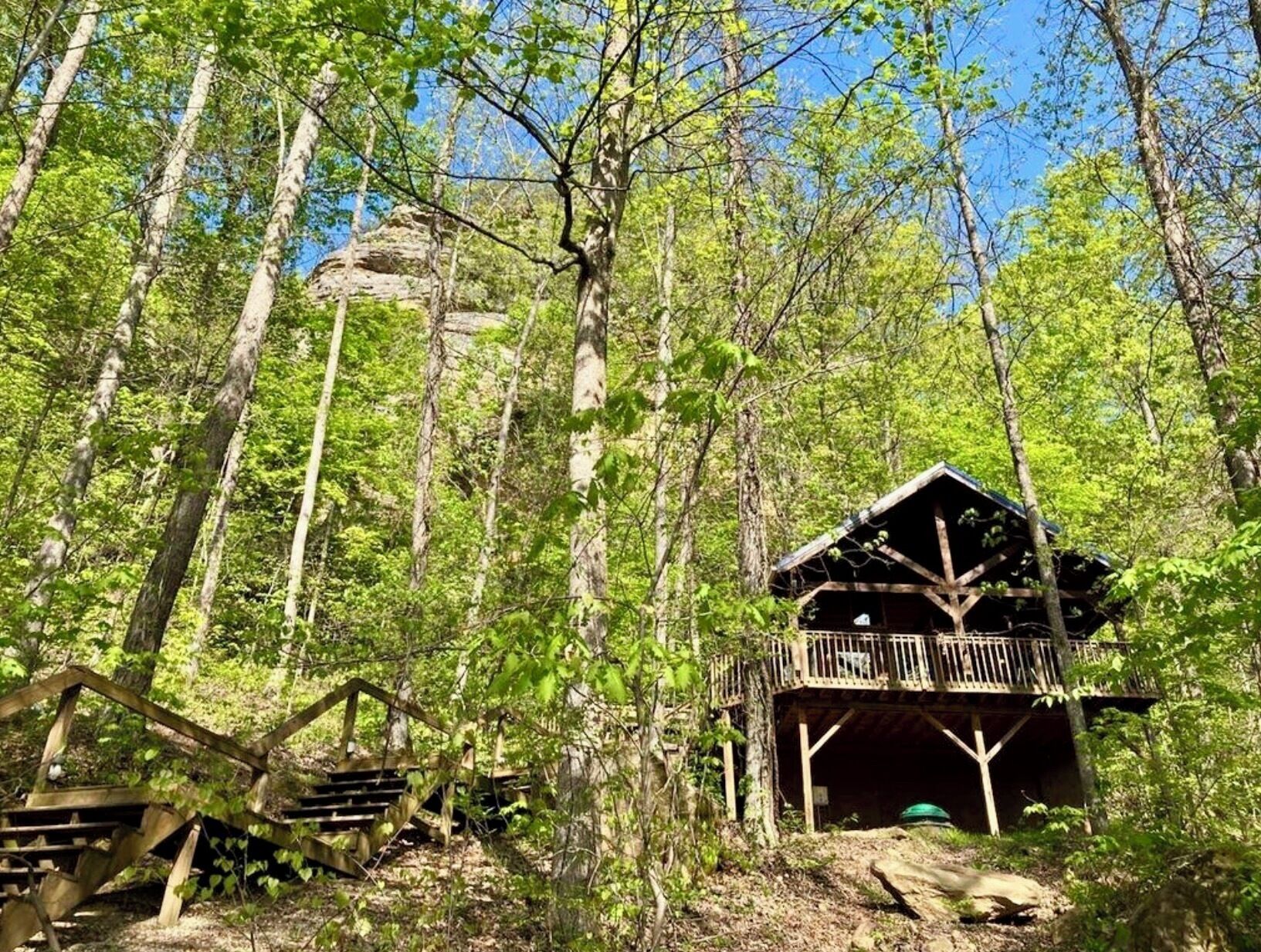 A rustic cabin with a wooden deck, surrounded by dense forest.
