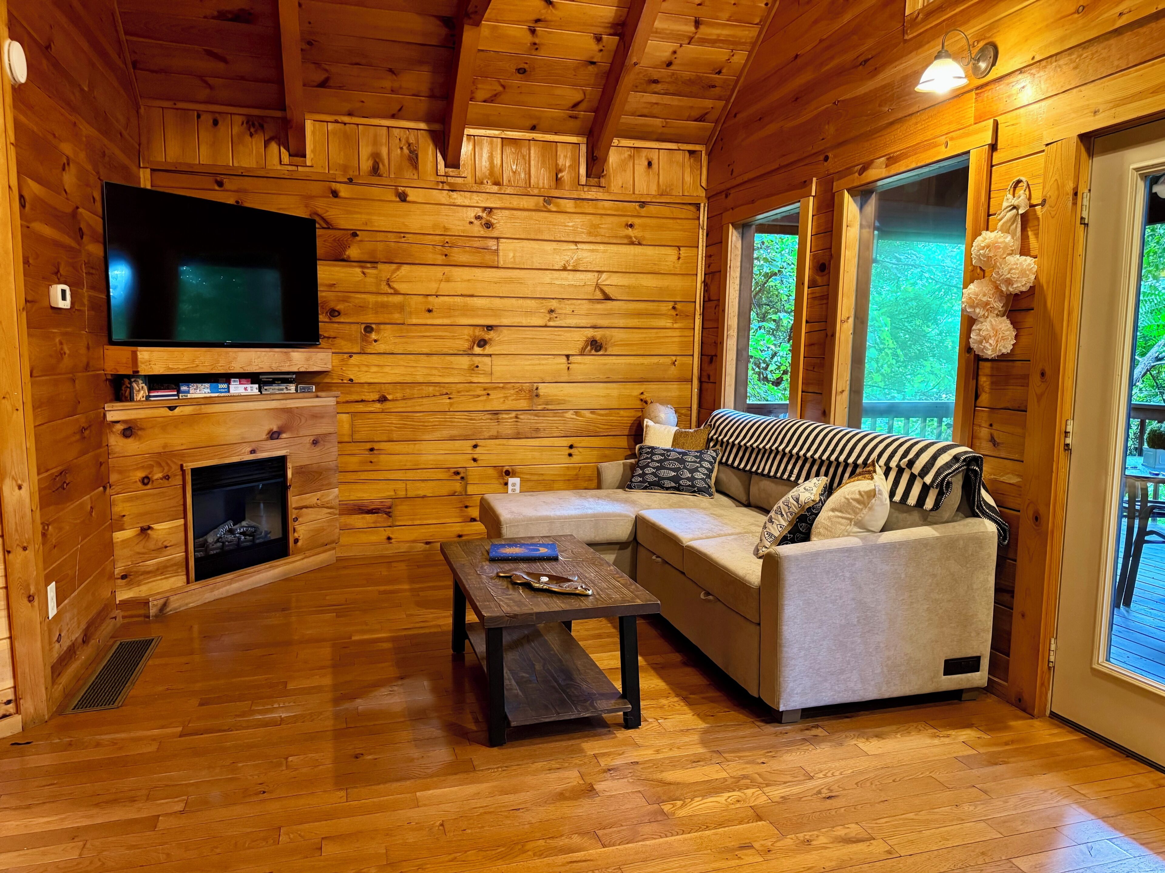 A log cabin interior with a fireplace, a television, a sofa, and a dining table.
