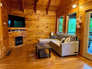 A log cabin interior with a fireplace, a television, a sofa, and a dining table.