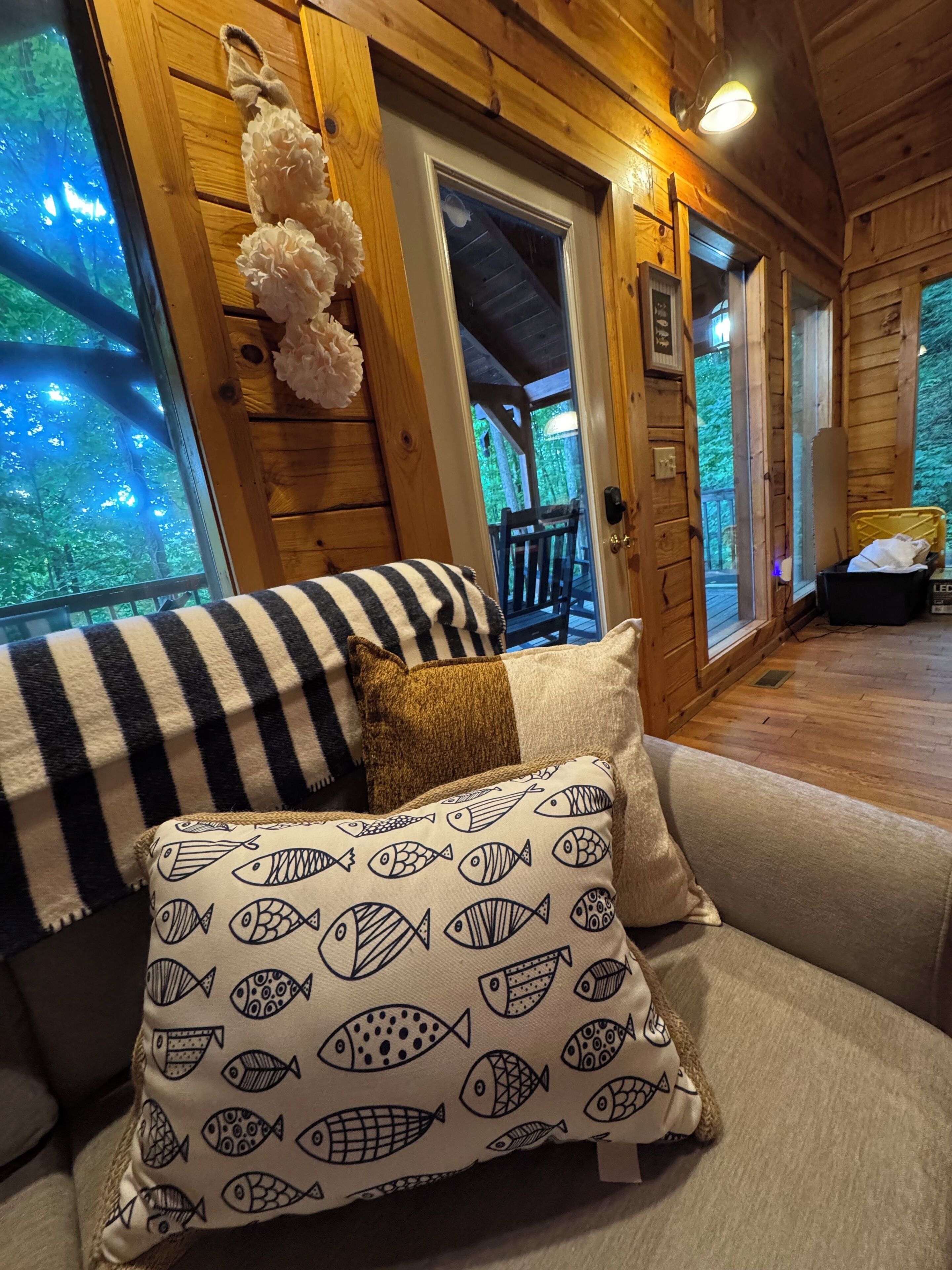 L’intérieur d’un chalet en bois, avec un canapé, des coussins à motifs et une vue sur l’extérieur.