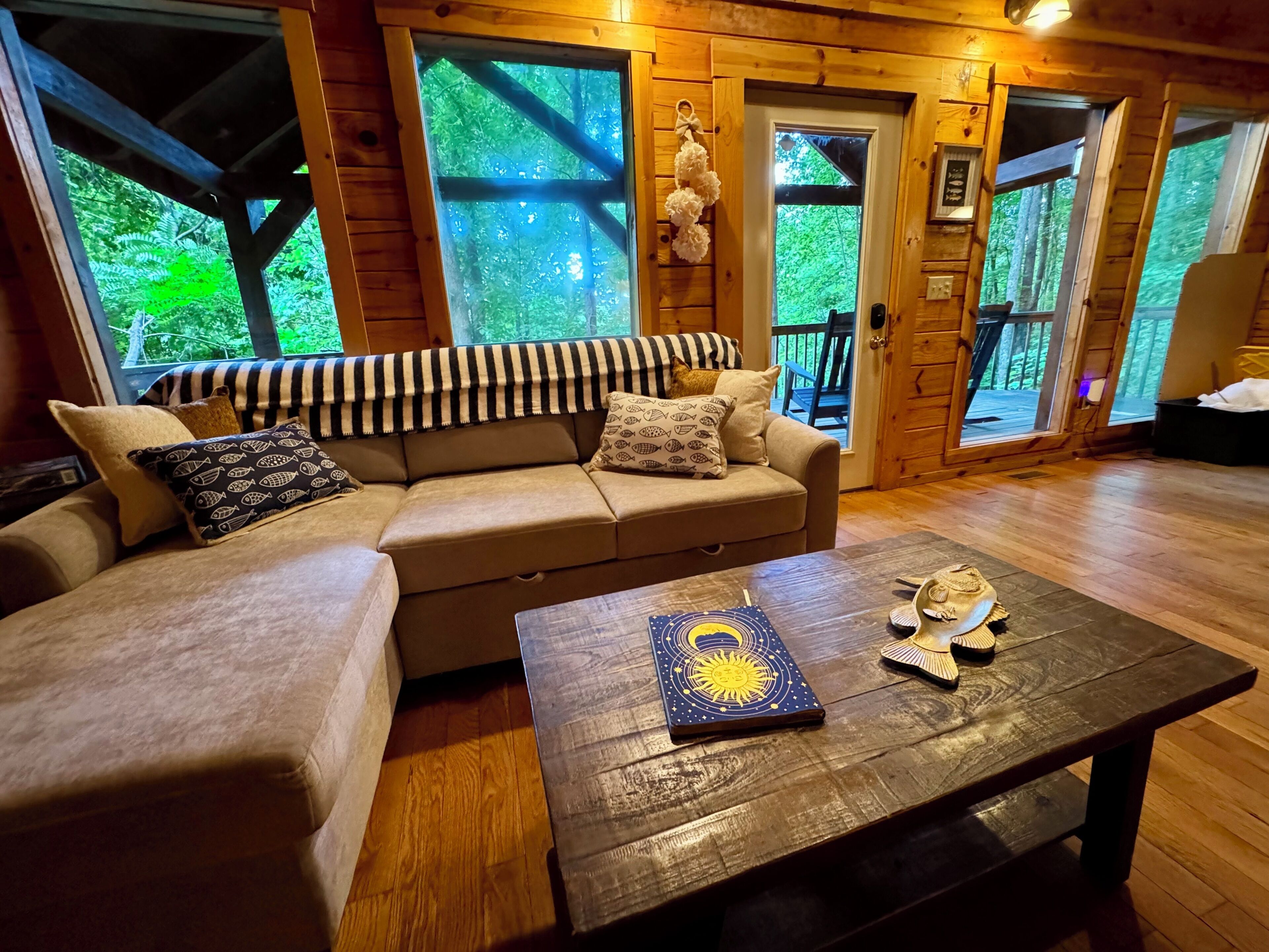 A cozy room with a sofa, a coffee table, and a view of the outdoors through large windows.