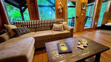 A cozy room with a sofa, a coffee table, and a view of the outdoors through large windows.