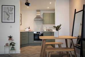 A modern kitchen with a wooden table and bench, green cabinets, and a herringbone floor pattern. - Pinot Perch | With FREE Underground Parking (Whitby)