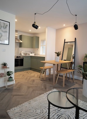 Une cuisine moderne avec des meubles de couleur verte, une table à manger avec des bancs, un grand miroir et un sol à motifs en chevrons.
