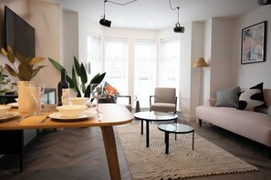 A modern living room with a sofa, a dining table set with plates, glasses, and a bottle, and a coffee table. - Pinot Perch | With FREE Underground Parking (Whitby)