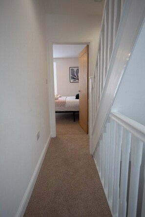 A hallway leading to a bedroom with a bed, a door, and a carpeted floor. - Sea Renity  - Whitby (Whitby)