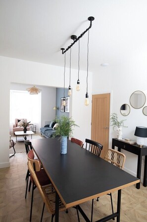 A modern dining area with a long table, chairs, hanging light fixtures, and a potted plant. - Sea Renity  - Whitby (Whitby)