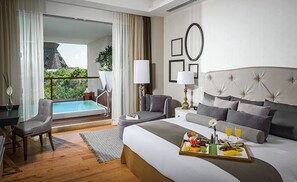 Una camera d'albergo con un letto, una scrivania, una sedia, un comodino, una lampada, un vassoio con la colazione e vista su una piscina e vegetazione.