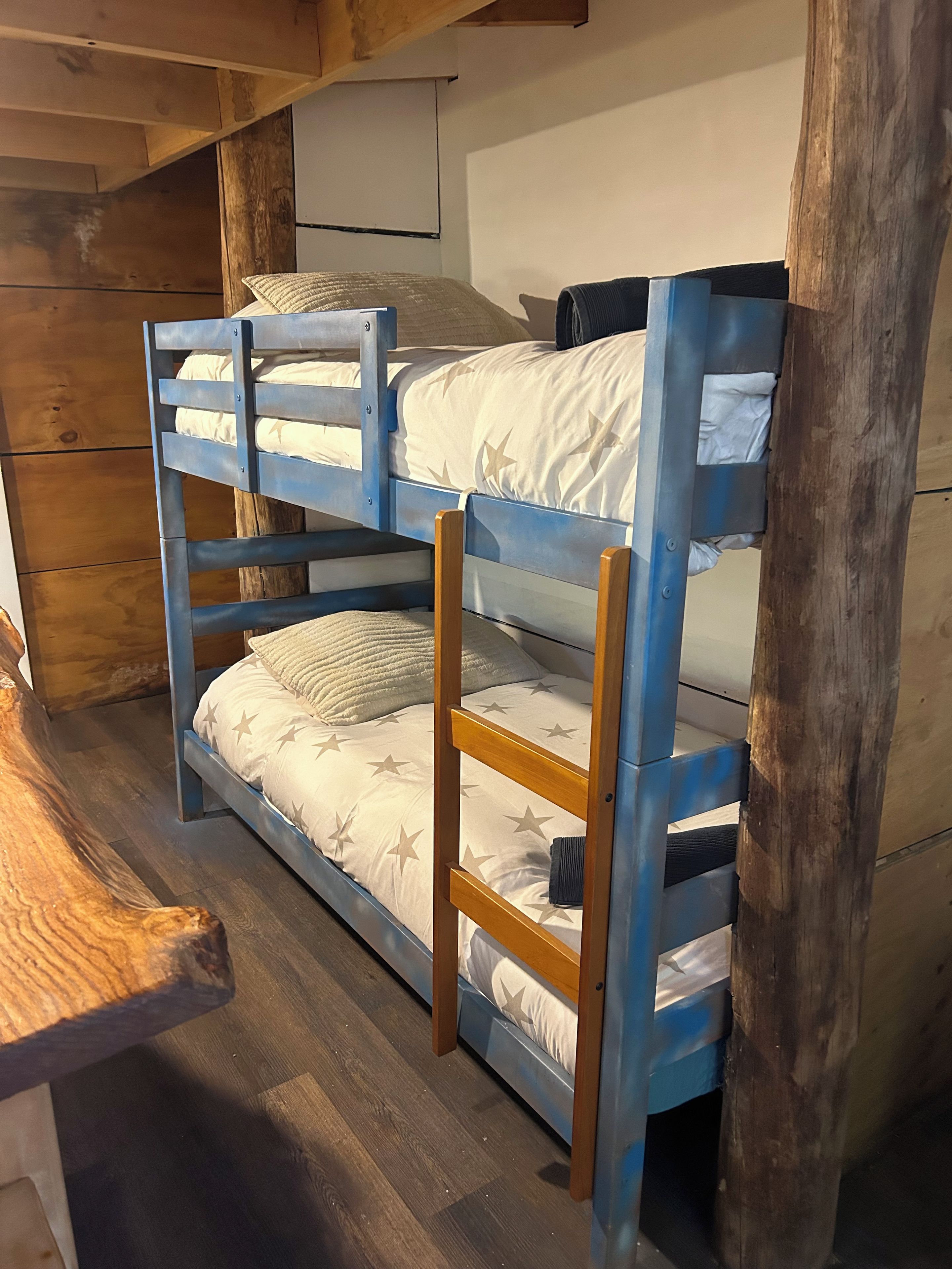 Un letto a castello con una scala in legno, un pavimento in legno e una parete bianca con una finestra.