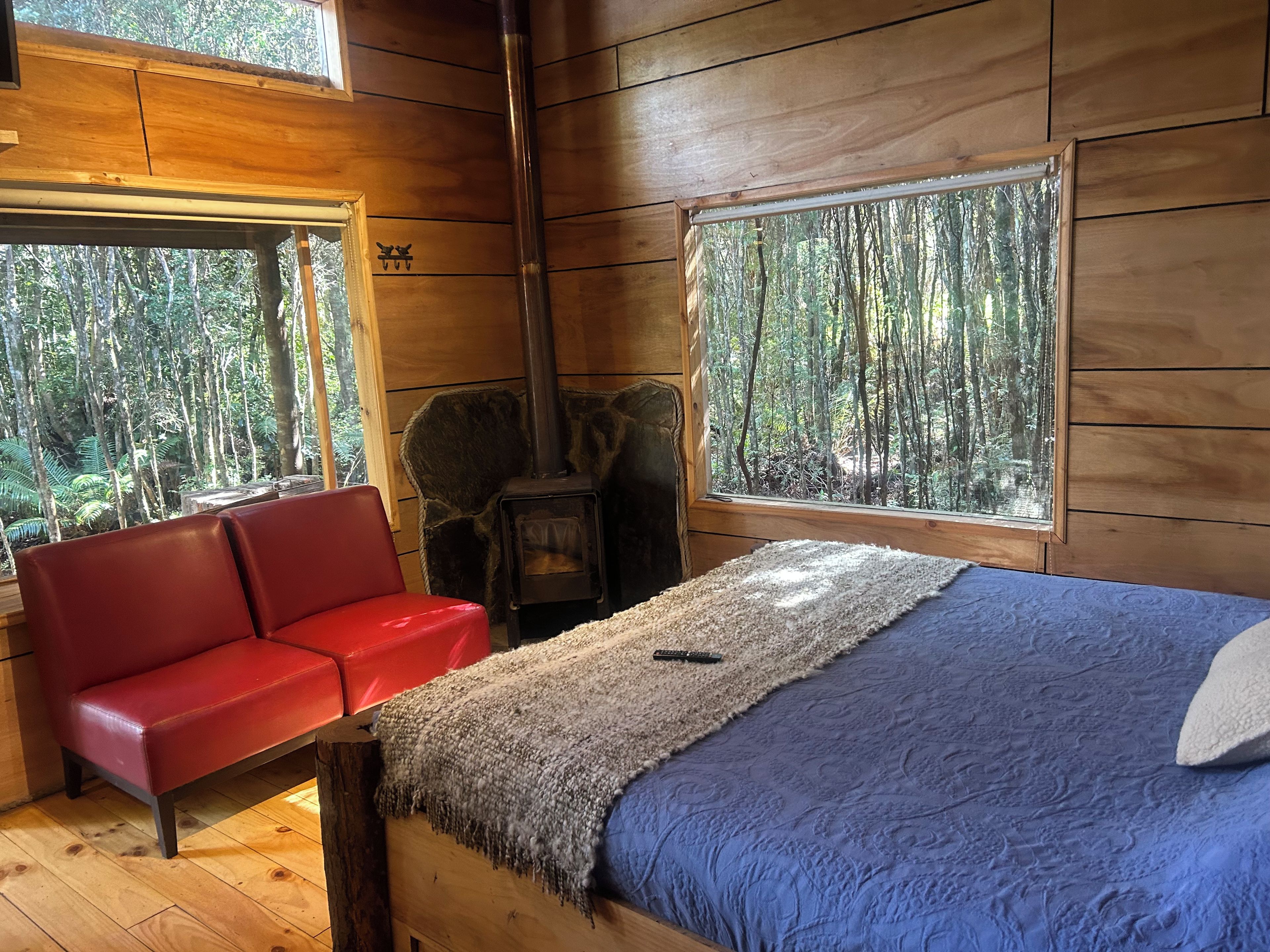 L'intérieur d'un chalet comprend un lit, un canapé rouge, une cheminée et de grandes fenêtres donnant sur la forêt.