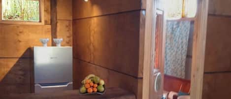 Interior de una cabaña de madera con mostrador de cocina, una ventana pequeña y una puerta que da al baño.