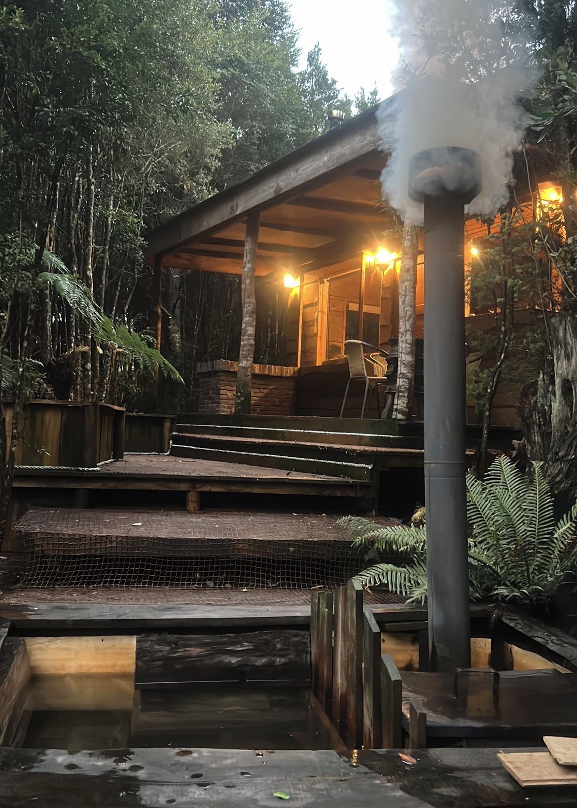 A rustic outdoor hot tub area with a wooden deck, surrounded by dense foliage.