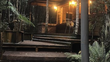 A rustic outdoor hot tub area with a wooden deck, surrounded by dense foliage.