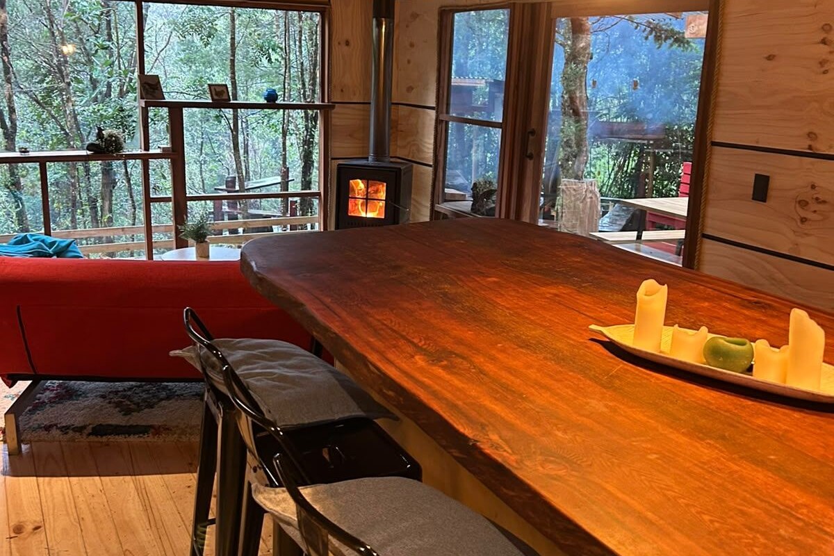 A cozy cabin interior with a wooden bar, seating area, and a wood-burning stove.