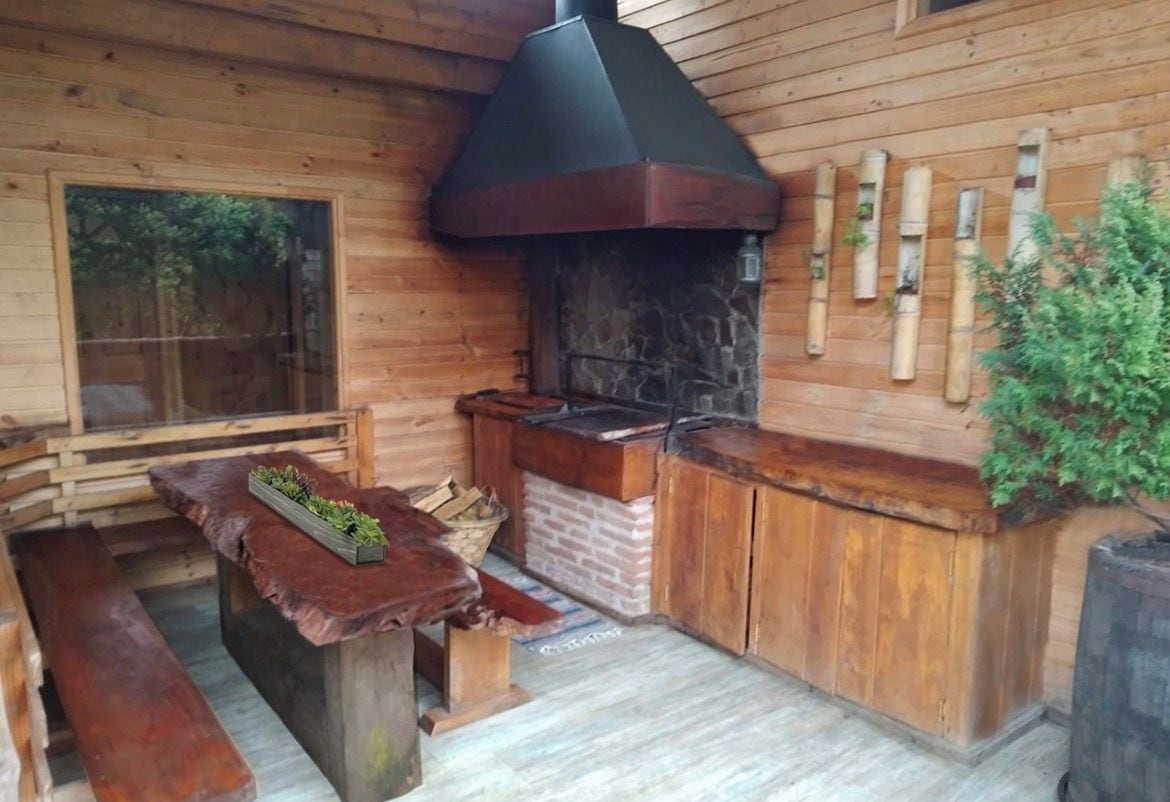 A wooden cabin interior with a stone fireplace, wooden benches, and a window overlooking a forest.