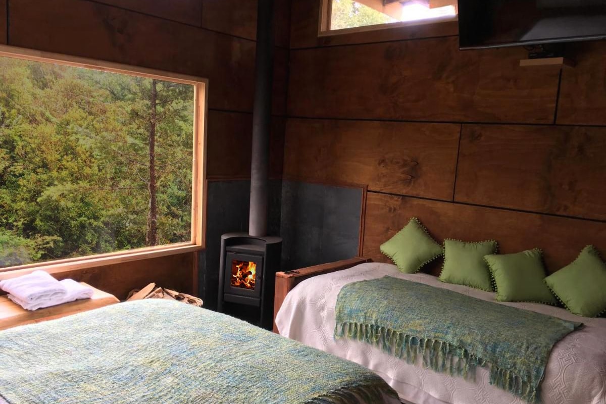 A cozy room with a bed, a window with a view of trees, and a wood-burning stove.