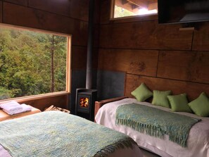 A cozy room with a bed, a window with a view of trees, and a wood-burning stove.