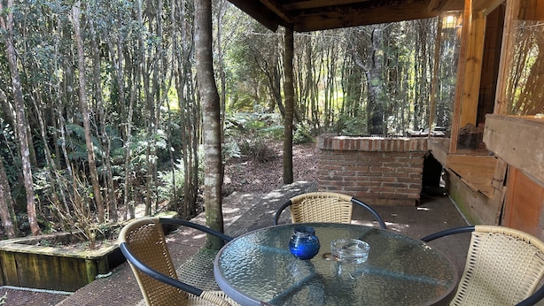 Eine Terrasse im Freien mit einem runden Glastisch und Korbstühlen, umgeben von einer hölzernen Pergola und einer Ziegelmauer.